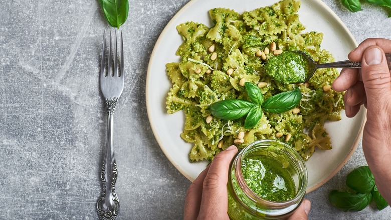 Person spooning pesto onto a plate of farfalle pasta