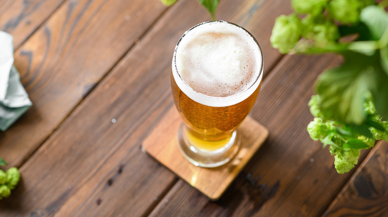 An overhead shot of a glass of light beer on a wooden table outdoors.