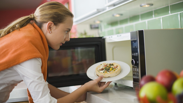 Person putting a plate of food into a microwave