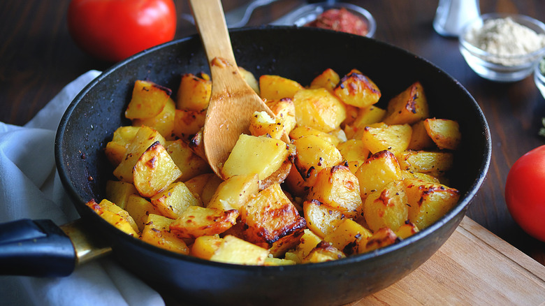 Fried potato chunks in a pan with wooden spoon