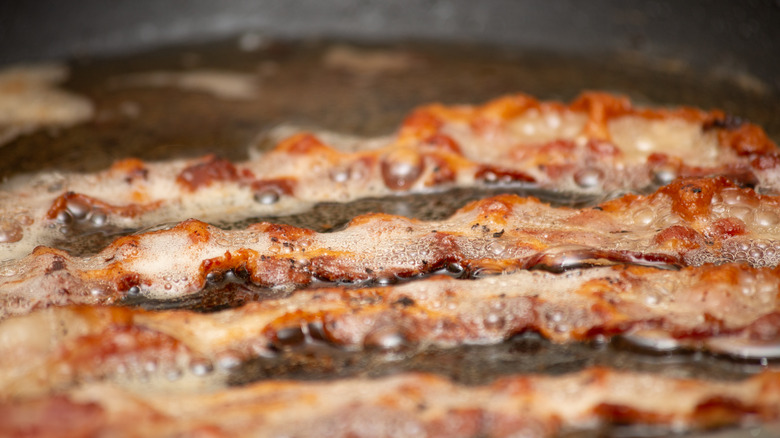 Bacon sizzling with water in a pan