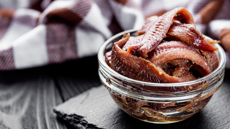 Anchovies in clear bowl on slate and wooden table