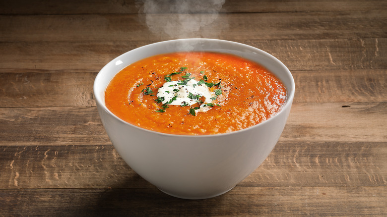 Bowl of reddish orange soup on table. 