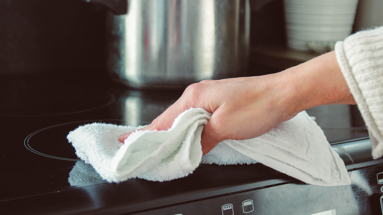 Hand wiping stovetop with cloth.