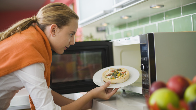 Woman putting pizza in microwave