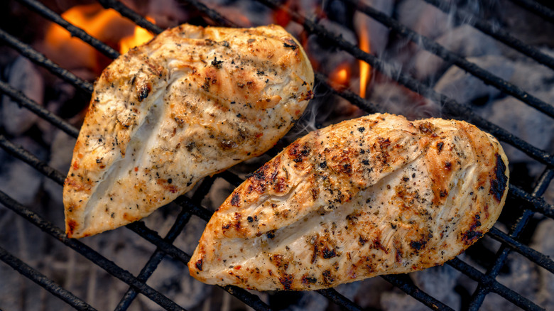 Deliciously seasoned and marinated chicken breasts, browned and with grill marks over the flame on a hot charcoal grill