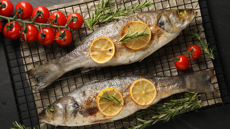 Whole fish on a baking rack with herbs, lemons, and cherry tomatoes