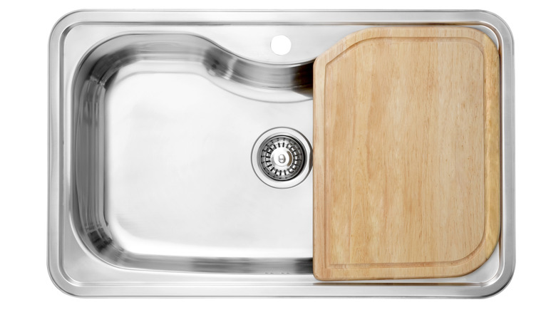 A stainless steel sink with a wooden cutting board on top
