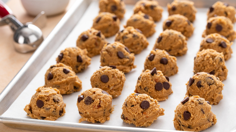 Scooped cookie dough balls on a baking tray next to an ice cream scoop