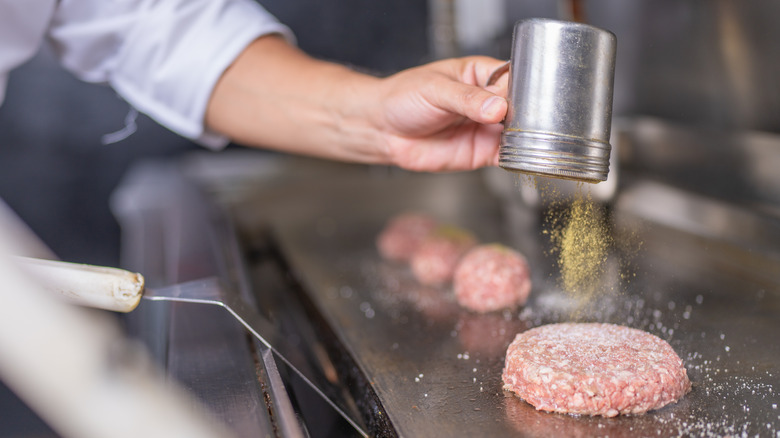 Person seasoning raw burger