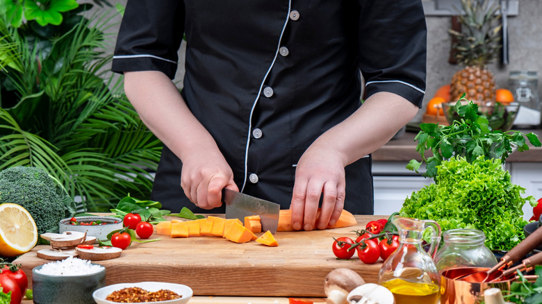 A chef cutting sweet potatoes with a Nakiri knife.