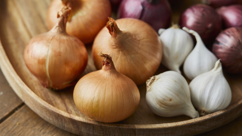 Onion varieties in closeup in a shallow wooden bowl.