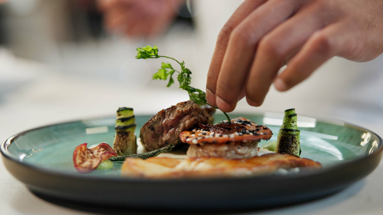 herbs being added to plate with meat and vegetables