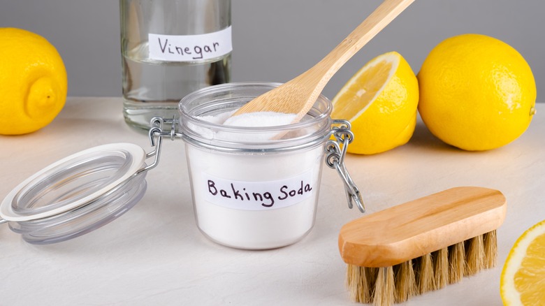 Baking soda, vinegar, lemons, and a scrub brush on white surface