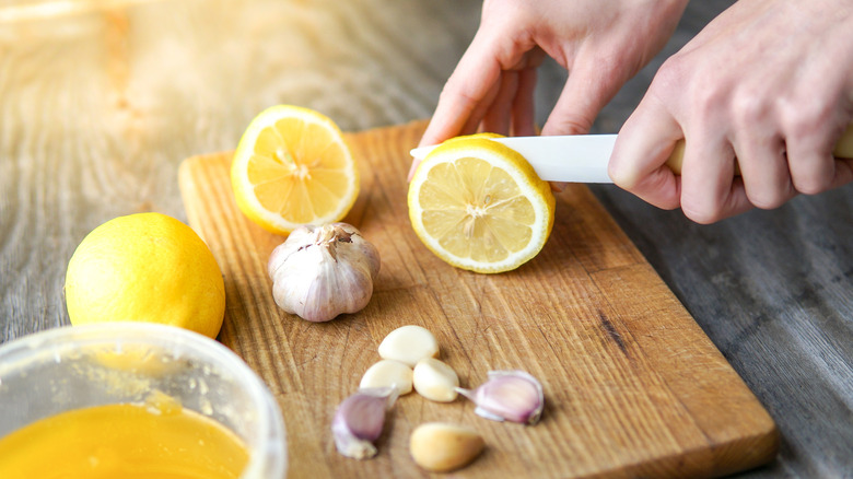 Hands chopping lemons and garlic on a wooden cutting board