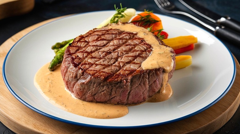 A cooked steak resting on a pool of creamy sauce on a white plate