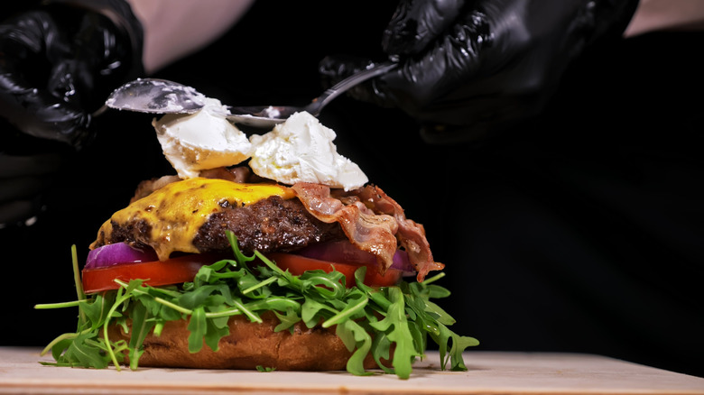 Chef adding ricotta to bacon cheeseburger