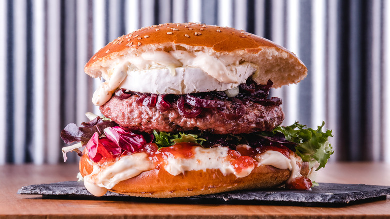 A burger with melted goat cheese, jam, caramelized onions, and greens