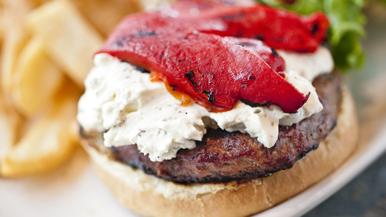 Roasted red peppers on top of a layer of goat cheese on a beef patty