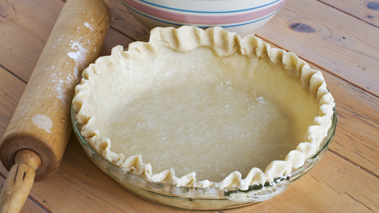 Pie dough in a pan with a rolling pin sitting beside it