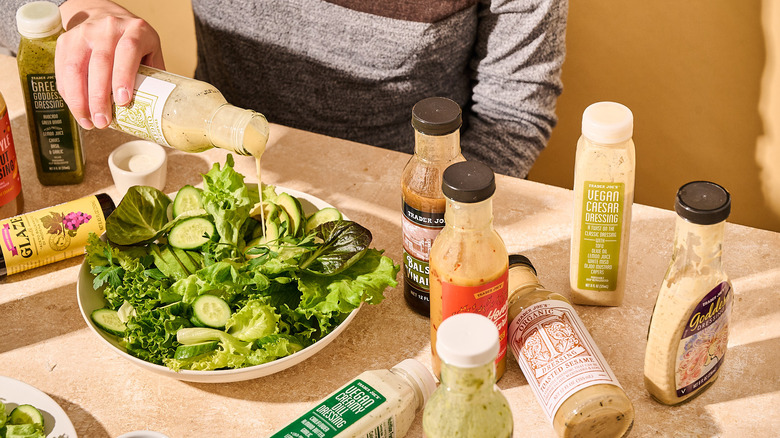 Man pouring salad dressing over salad surrounded by dressing bottles