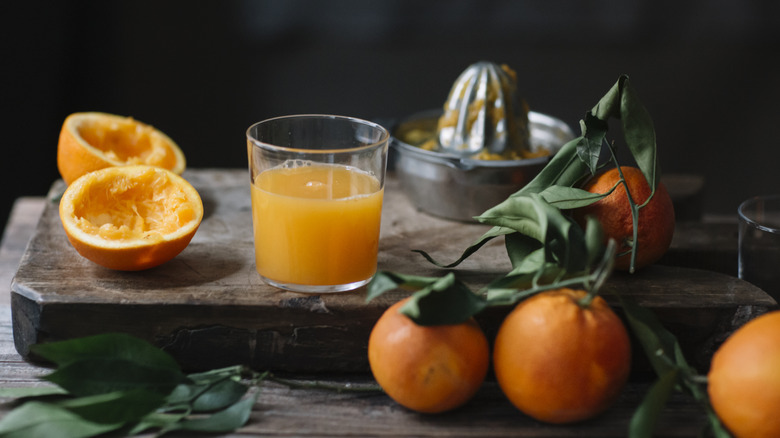 Orange juice and fresh-squeezed oranges on wood cutting board