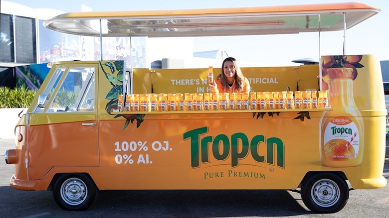 Bottles of "Tropcn" orange juice in an orange "Tropcn" bus at at CES 2024.