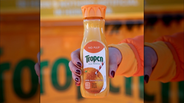 Hand holding bottle of "Tropcn" orange juice. 