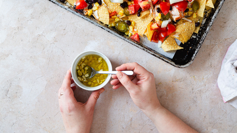 hand mixing garlic oil beside nachos pan