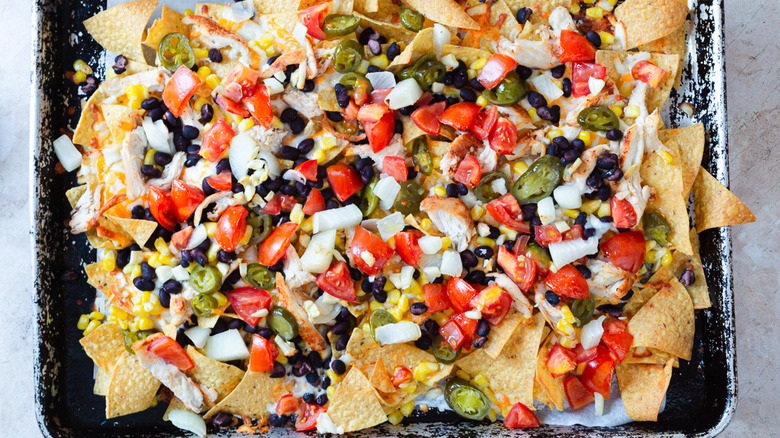 Unbaked nachos with toppings in baking sheet
