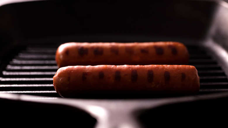 Two golden-brown hot dogs cooking on a cast iron griddle