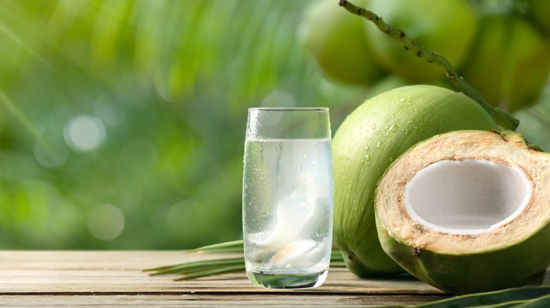 a glass of coconut water with coconuts in background