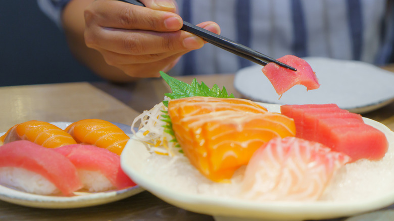 Raw tuna and salmon sit on a plate while a piece is picked up