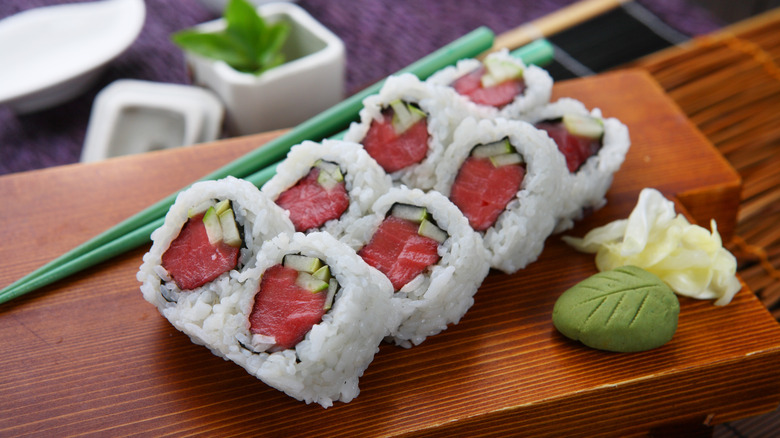 Tuna rolls sit on a wood block next to chopsticks