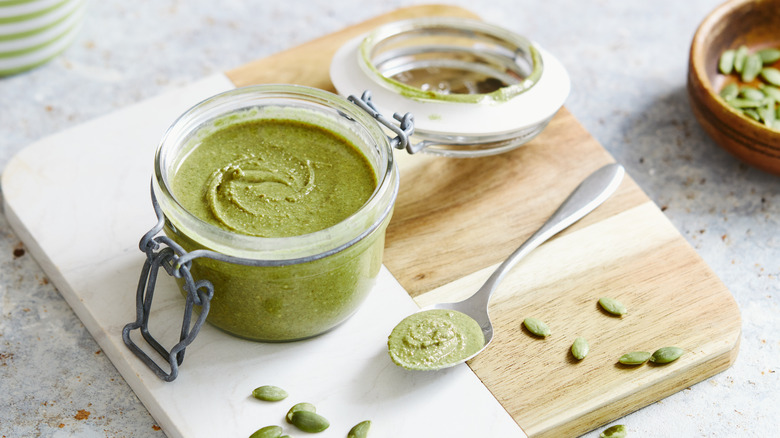 An open jar of pumpkin seed butter and a spoon rest on cutting board.