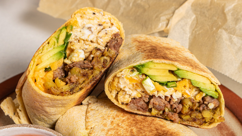 breakfast burritos with eggs, sausage, and avocado, sliced and standing