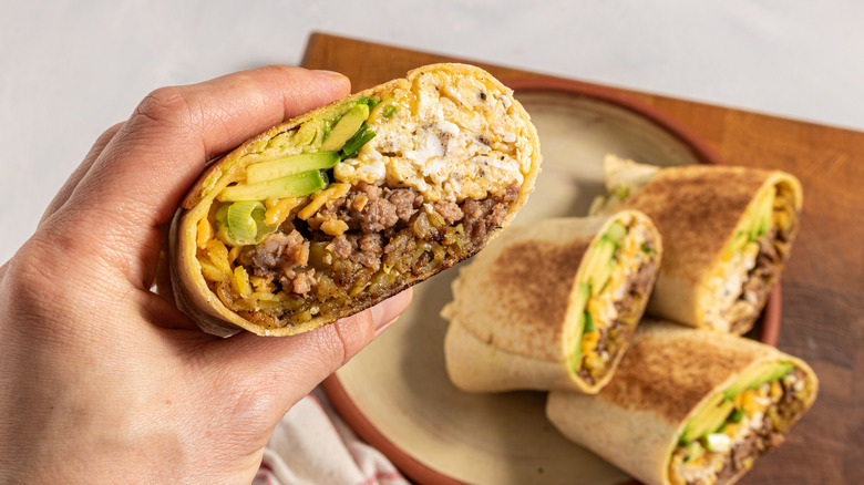 hand holding breakfast burrito with eggs, sausage, and avocado