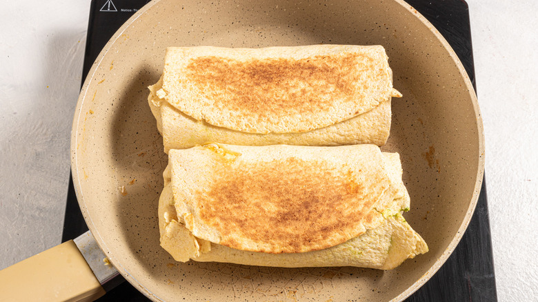 Two burritos browning in a skillet