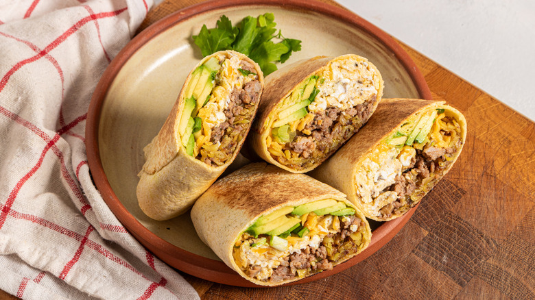 breakfast burritos with eggs, sausage, and avocado, sliced and standing