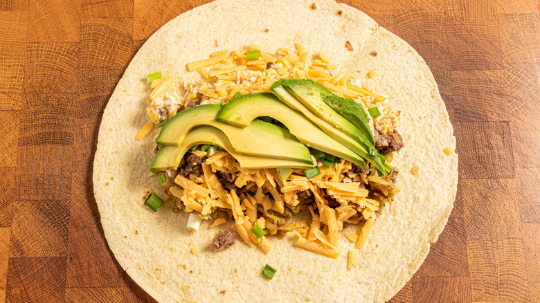 Tortilla filled with shredded cheddar, chopped green onions, and slices of avocado