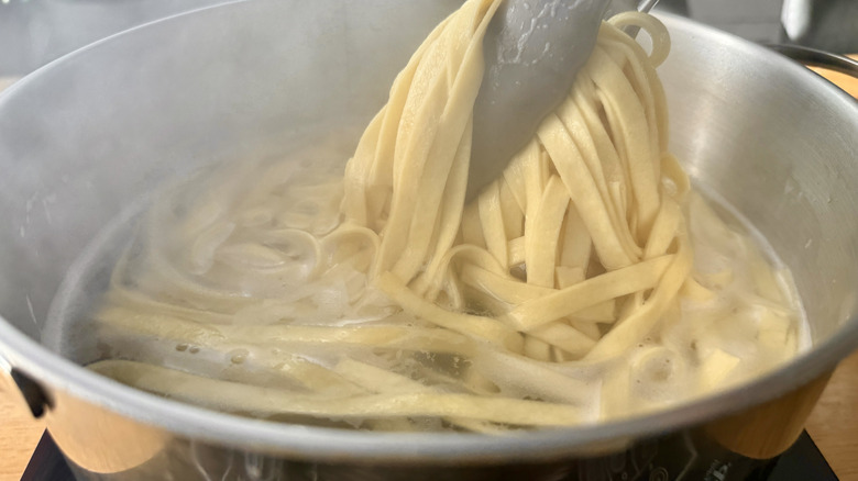 Tongs pulling pasta out of boiling water