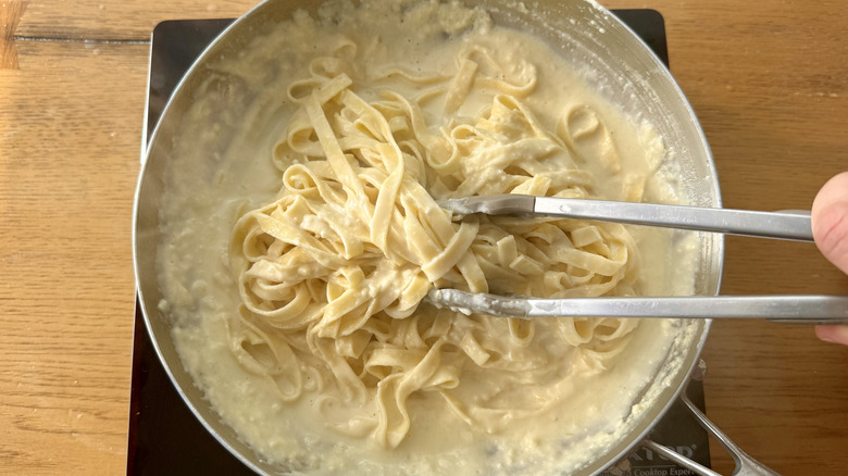 Tongs mixing pasta into creamy sauce