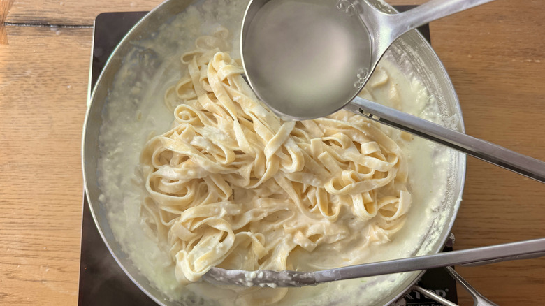 Ladle of water pouring onto fettuccine Alfredo in pan