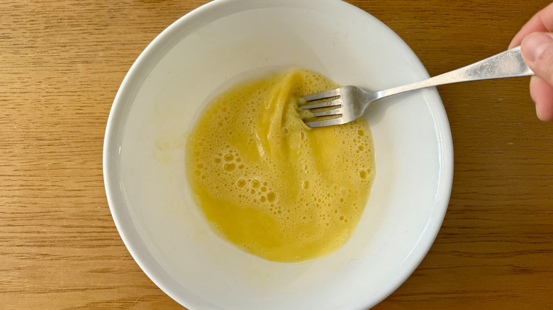 Fork whisking egg in white bowl