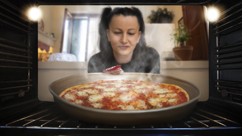 Woman looking at pizza in oven