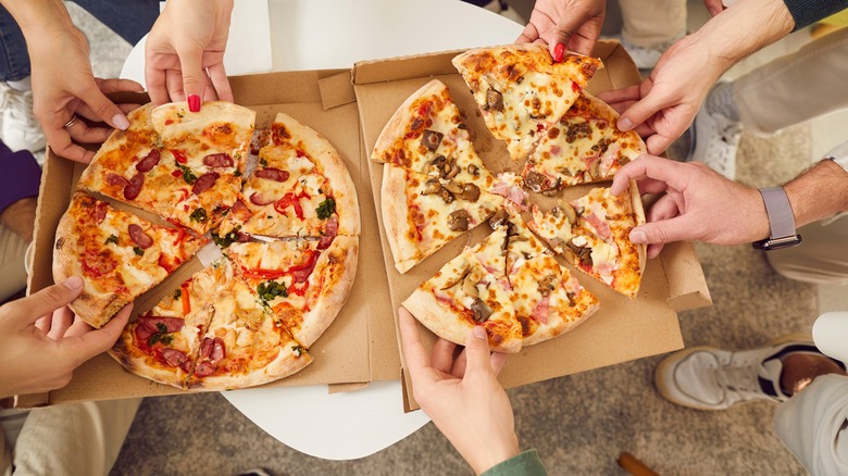 Hands splitting two boxes of pizza