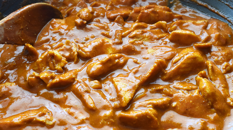 Stirring chicken with butter sauce in pan before it goes in a slow cooker
