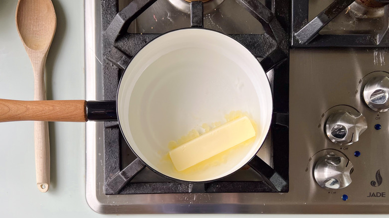 Butter stick, salt and water in saucepan on stove with wooden spoon