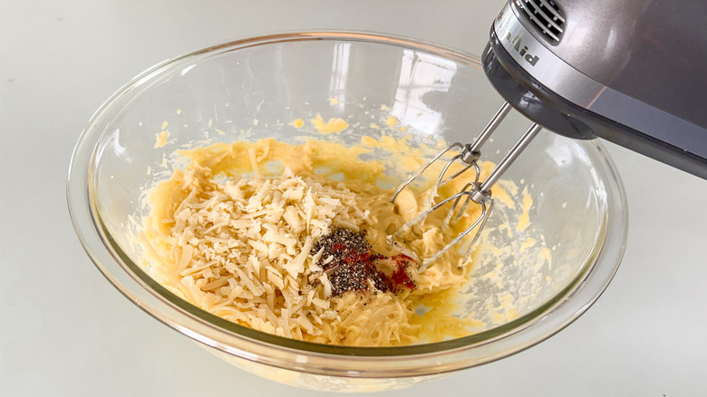 Using hand mixer to add cheese, pepper, and smoked paprika to gougerè dough in mixing bowl