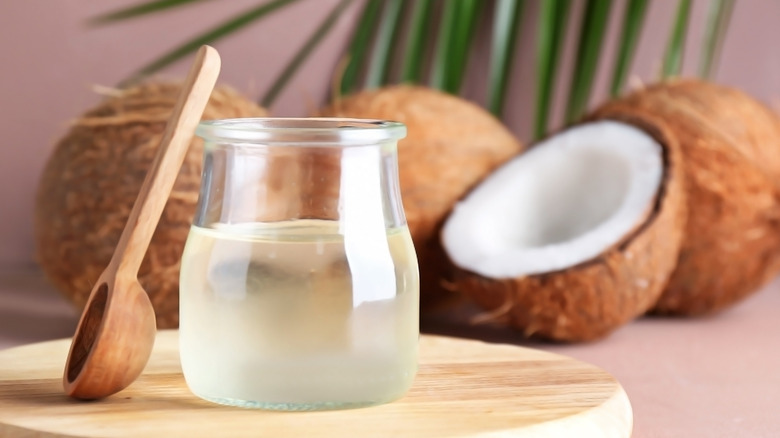 Jar of coconut oil with spoon and group of four coconuts in background